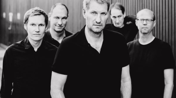 Schwarzweiß-Foto der Band, aufgenommen draußen. Die 5 Männer tragen schwarze Oberteile und gucken ernst in die Kamera