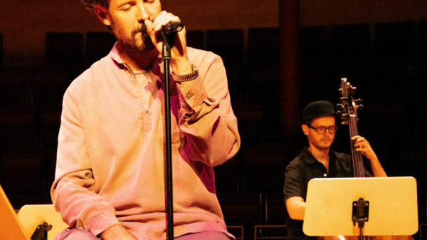 Max Herre sitzt und singt mit geschlossenen Augen, im Hintergrund spielt ein Mann Kontrabass