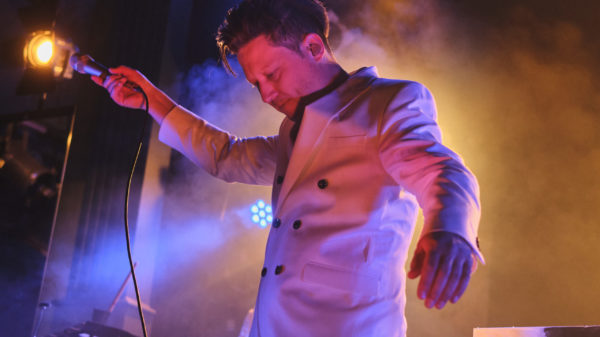 Dunkles Bild von der Bühne, rotes und blaue Lichter, Grober tanzt mit Mikrofon zur Seite