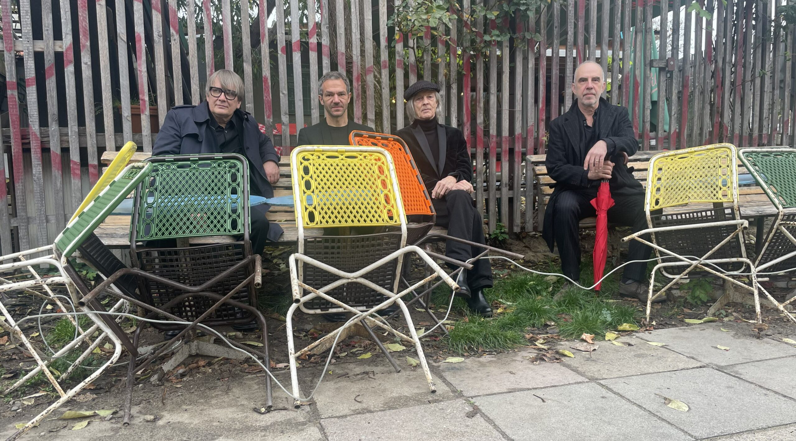 Die vier Musiker sitzten auf Holzbänken, vor ihnen stehen und lehnen so alte wie bunte Gartenstühle