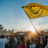 Festivalgelände, Sonnenuntergang, viele Menschen, einer Mann schwenkt vorne eine gelbe Fahne mit einem Smiley
