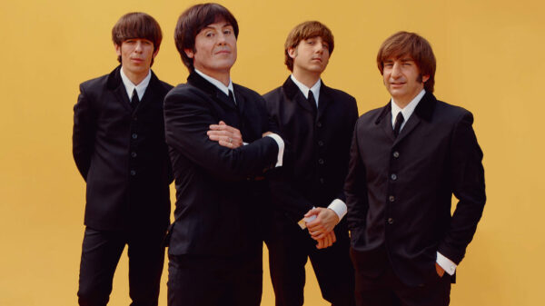 Vier Männer, die aussehen wie die jungen Beatles, in schwarzen Anzügen vor gelbem Hintergrund