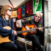 Laura-Mary Carter und Steven Ansell mit Gitarren und Sonnenbrillen an einem Flastock-Stand