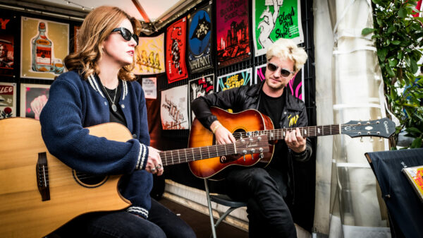 Laura-Mary Carter und Steven Ansell mit Gitarren und Sonnenbrillen an einem Flastock-Stand