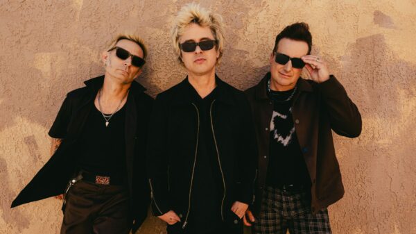 Die drei Musiker vor einer Wand, alle tragen Sonnenbrillen und schwarze Kleidung