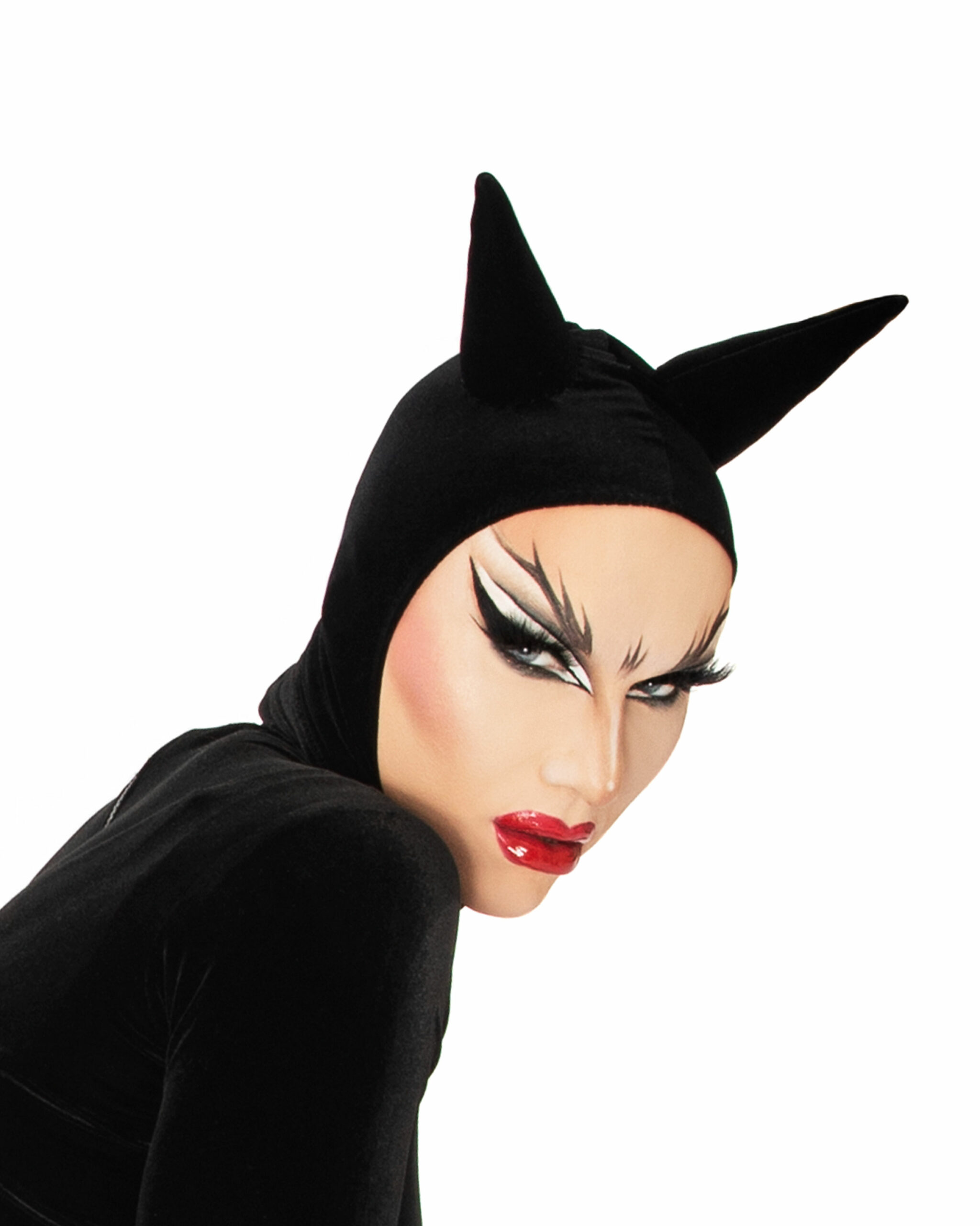 Sasha Velour trägt ein schwarzes Kostüm mit spitzen "Ohren" und ist unter anderem mit roten Lippen und auffälligem Augen-Make-up geschminkt