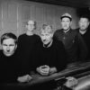 Schwarzweißfoto der Band, die fünf Musiker stehen beziehungsweise lehnen an einem Tresen in einer Kneipe