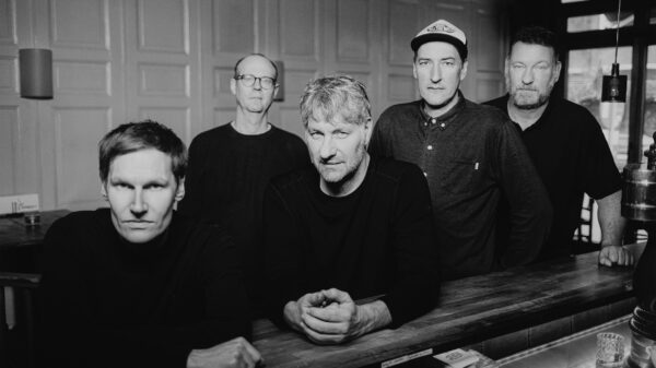 Schwarzweißfoto der Band, die fünf Musiker stehen beziehungsweise lehnen an einem Tresen in einer Kneipe