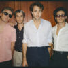 Die vier Männer tragen Hemden, stehen vor einer Holzwand und blicken in die Kamera