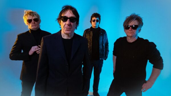 Vier Bandmitglieder vor blauem Hintergrund, alle mit Sonnenbrillen
