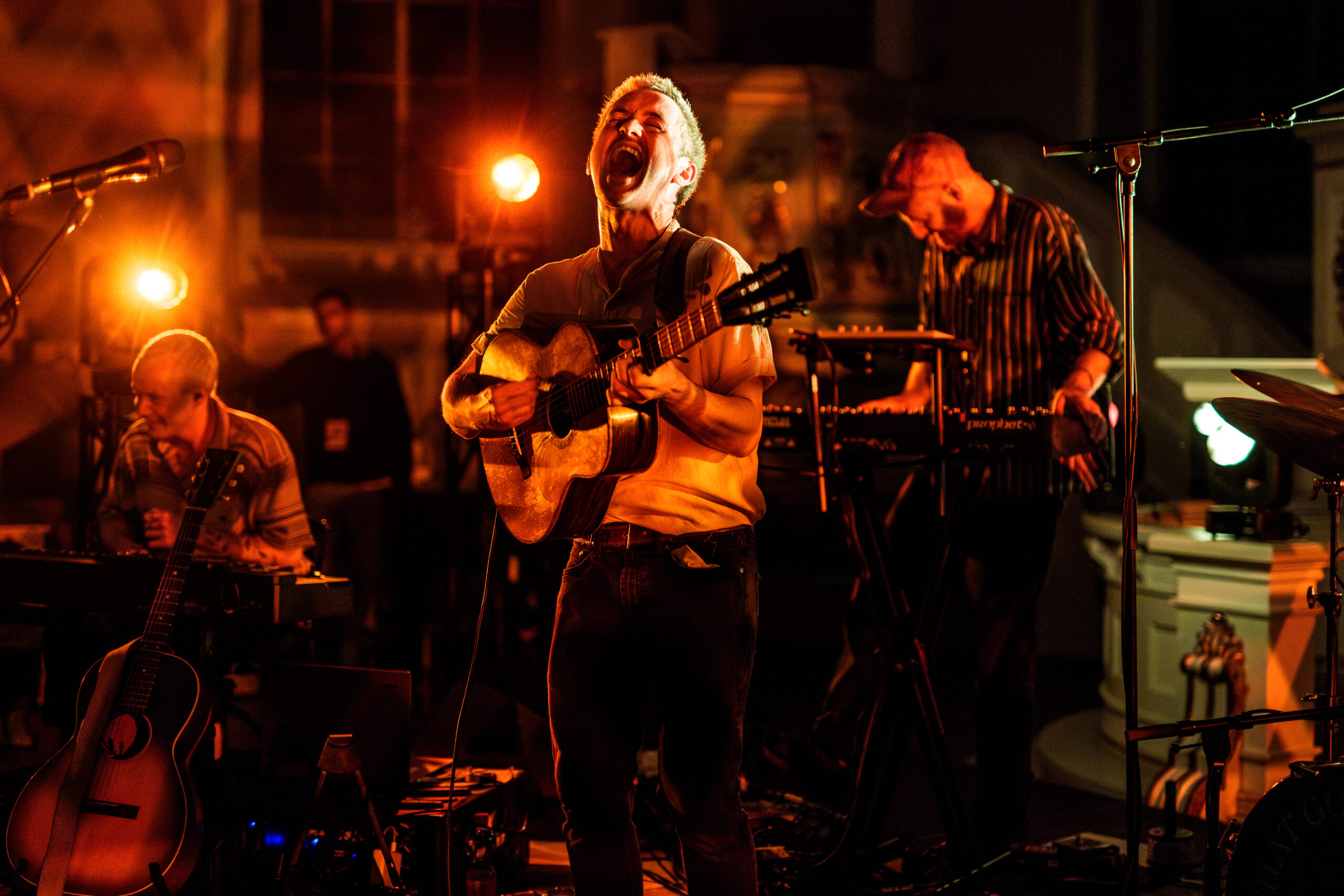 Vorne O'Brien mit Gitarre und aufgerissenem Mund, im Hintergrund zwei Musiker