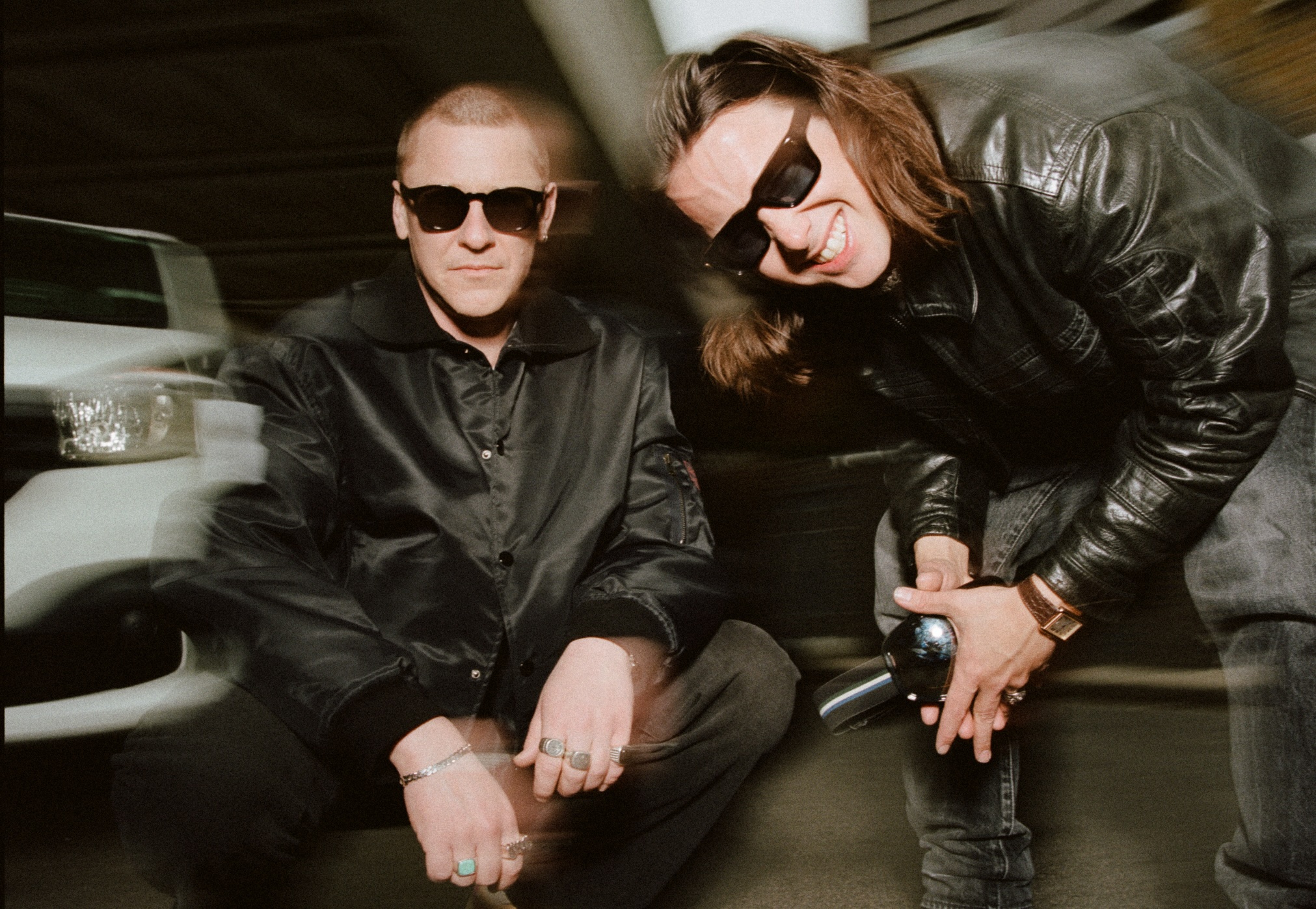 Foto in Teilen unscharf, beide mit schwarzen Oberteilen und Sonnenbrillen