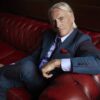 Paul Weller sitzt im Anzug auf einem roten Sofa