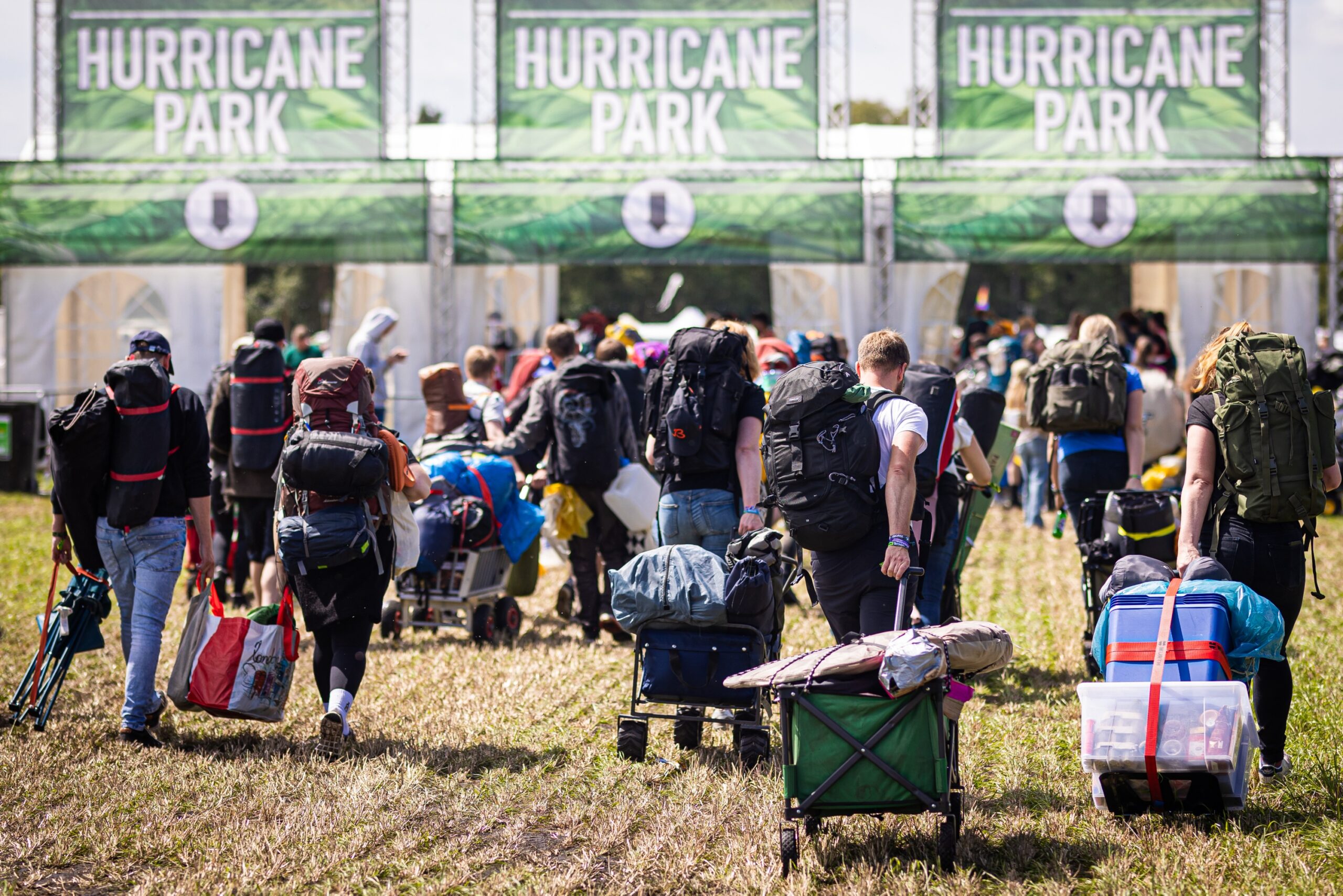 Menschen mit Rucksäcken ziehen und tragen ihr Gepäck über einen abgemähten Acker