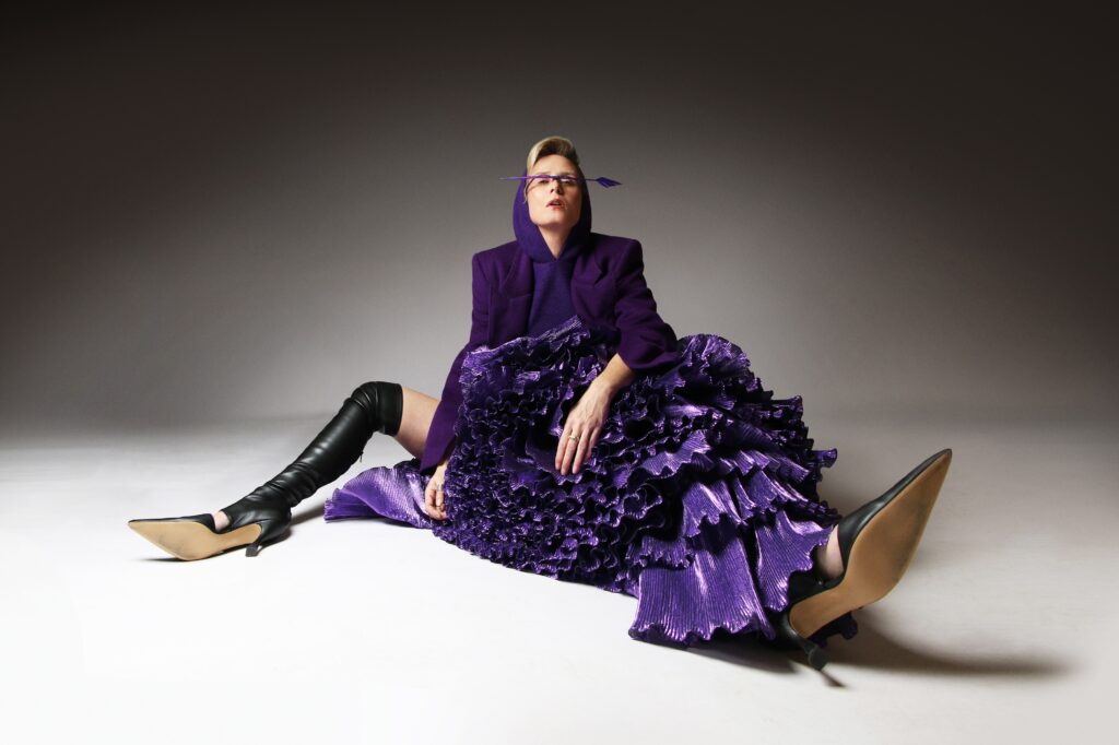 Sie sitzt in einem extravaganten lilafarbenen Outfit auf dem Boden