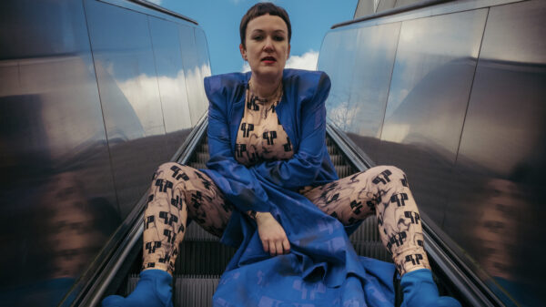 Sie sitzt in einem blauen Kleid und mit blauen Schuhen auf einer Rolltreppe