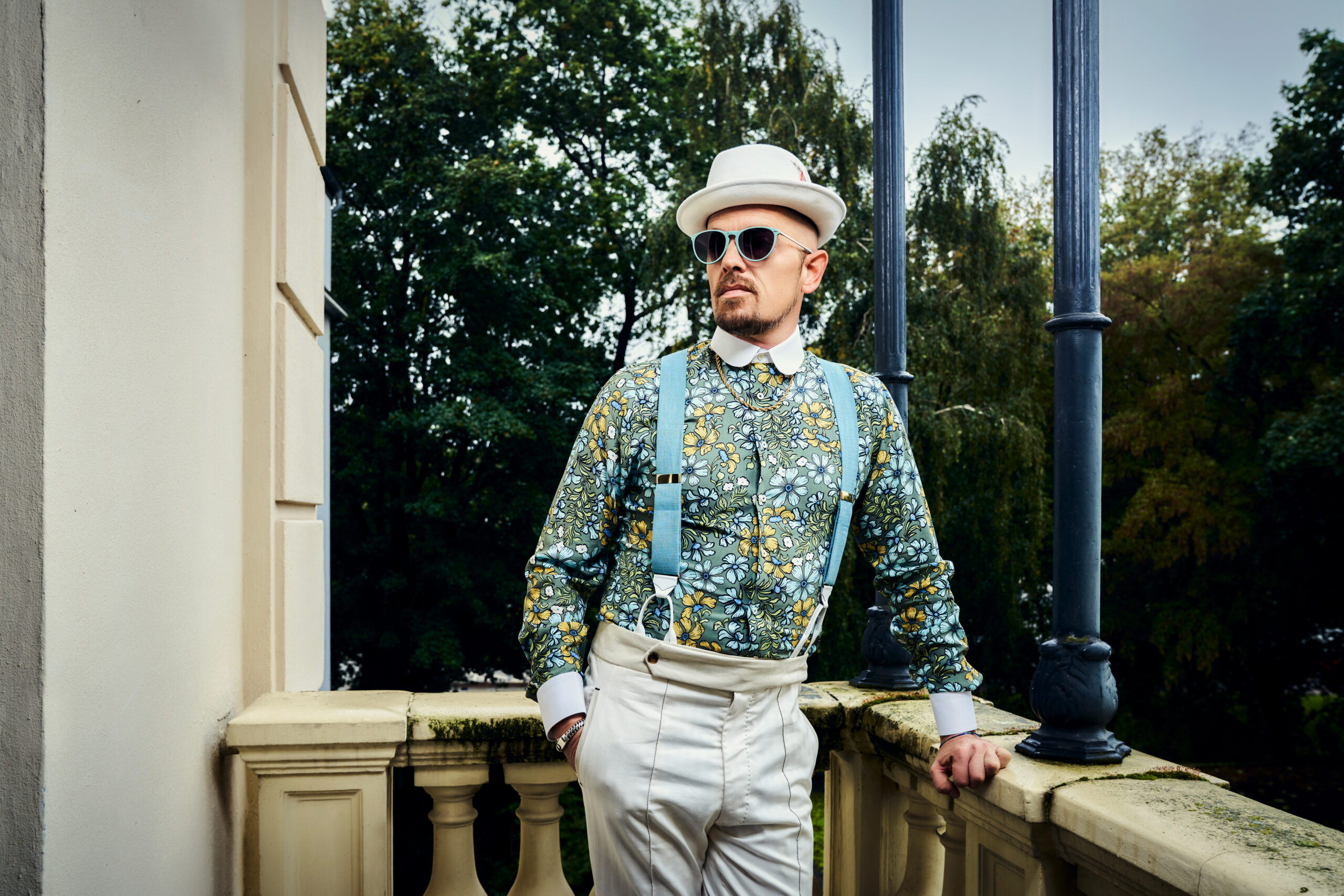 Jan Delay steht auf einem Balkon, trägt Hut, Sonnenbrille und ein Hemd mit Blümchen. Er schaut an der Kamera vorbei