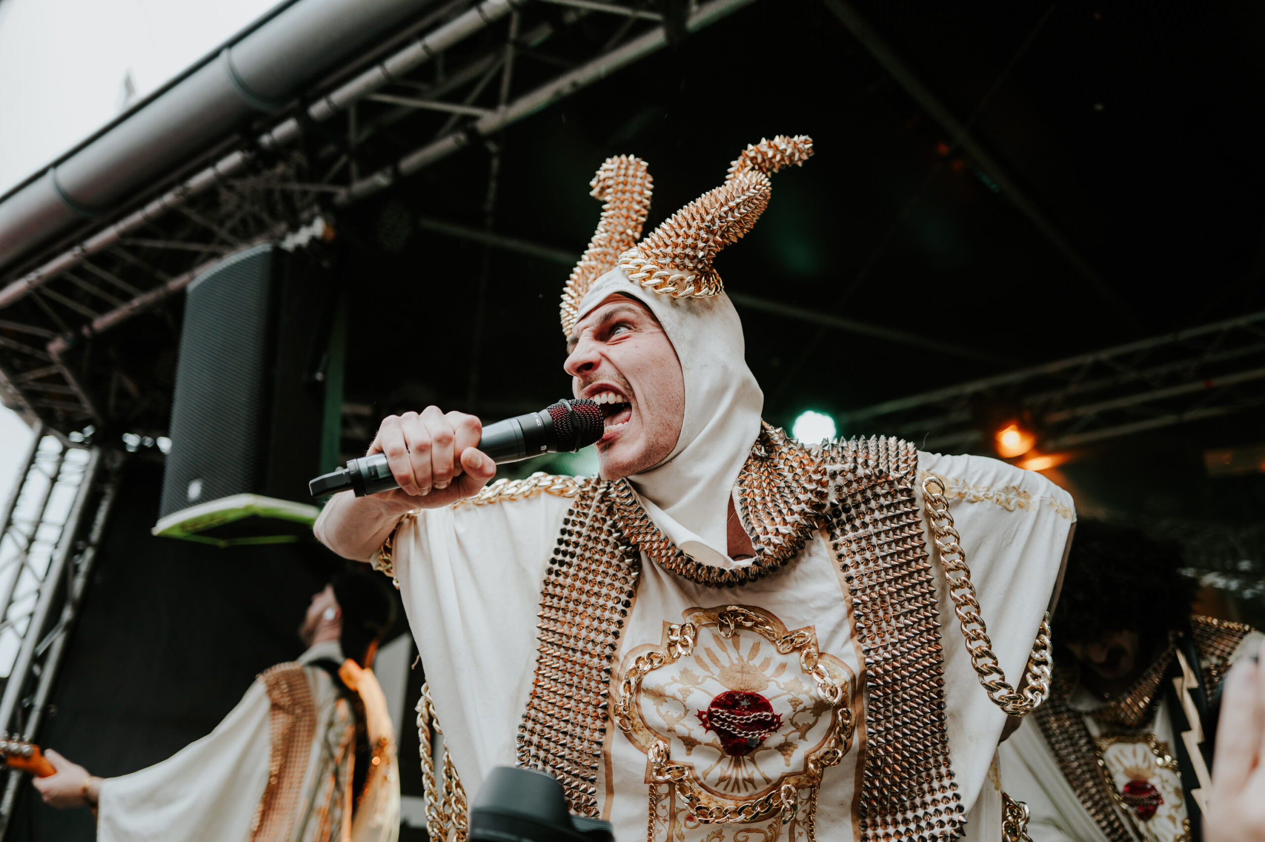 Band auf der Bühne, der Sänger trägt ein Kostüm mit vielen Ketten und Nieten und Hörner auf dem Kopf aus Ketten und Nieten
