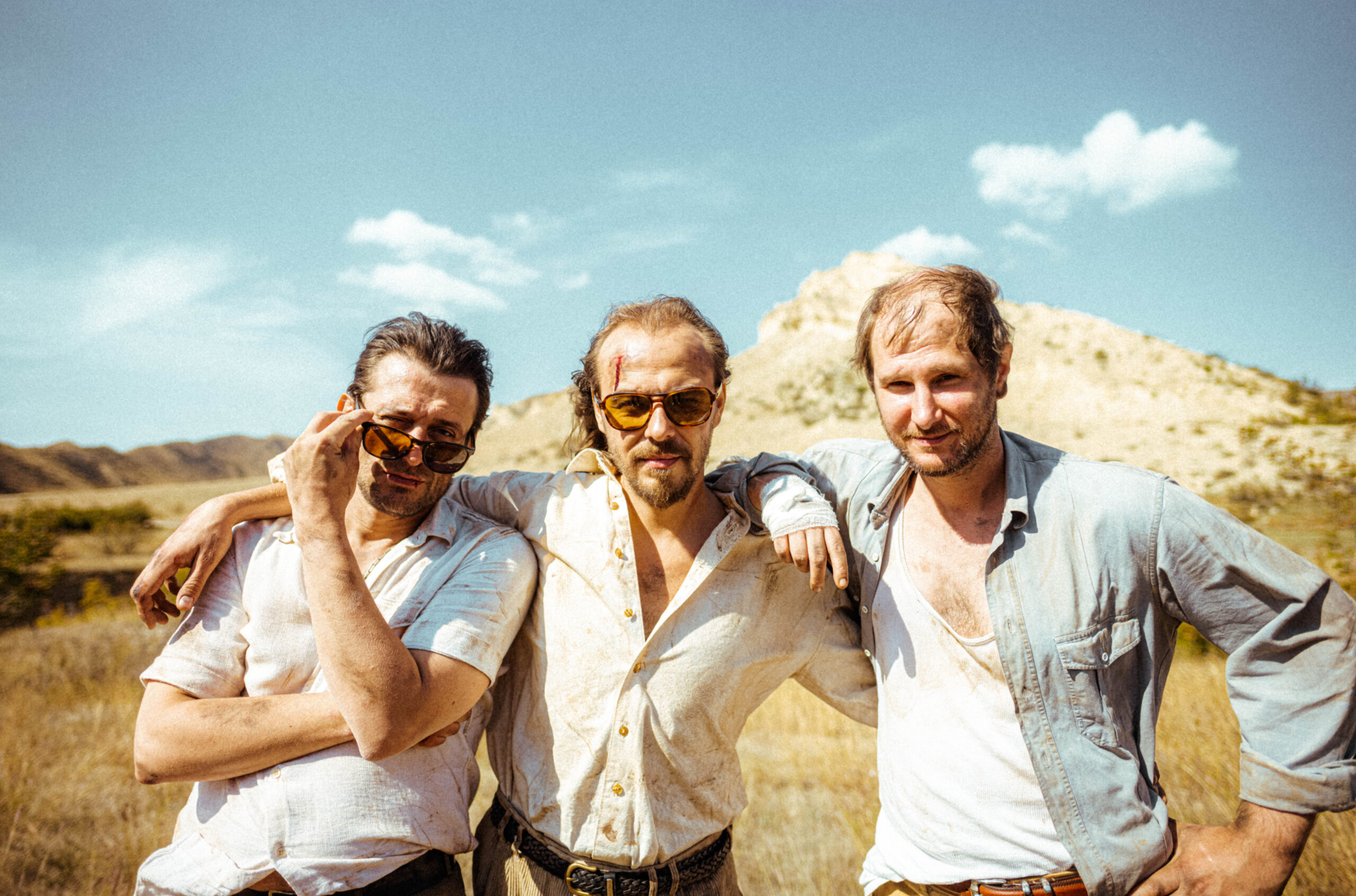 Drei Männer draußen, der Mann in der Mitte umarmt die beiden anderen Männer