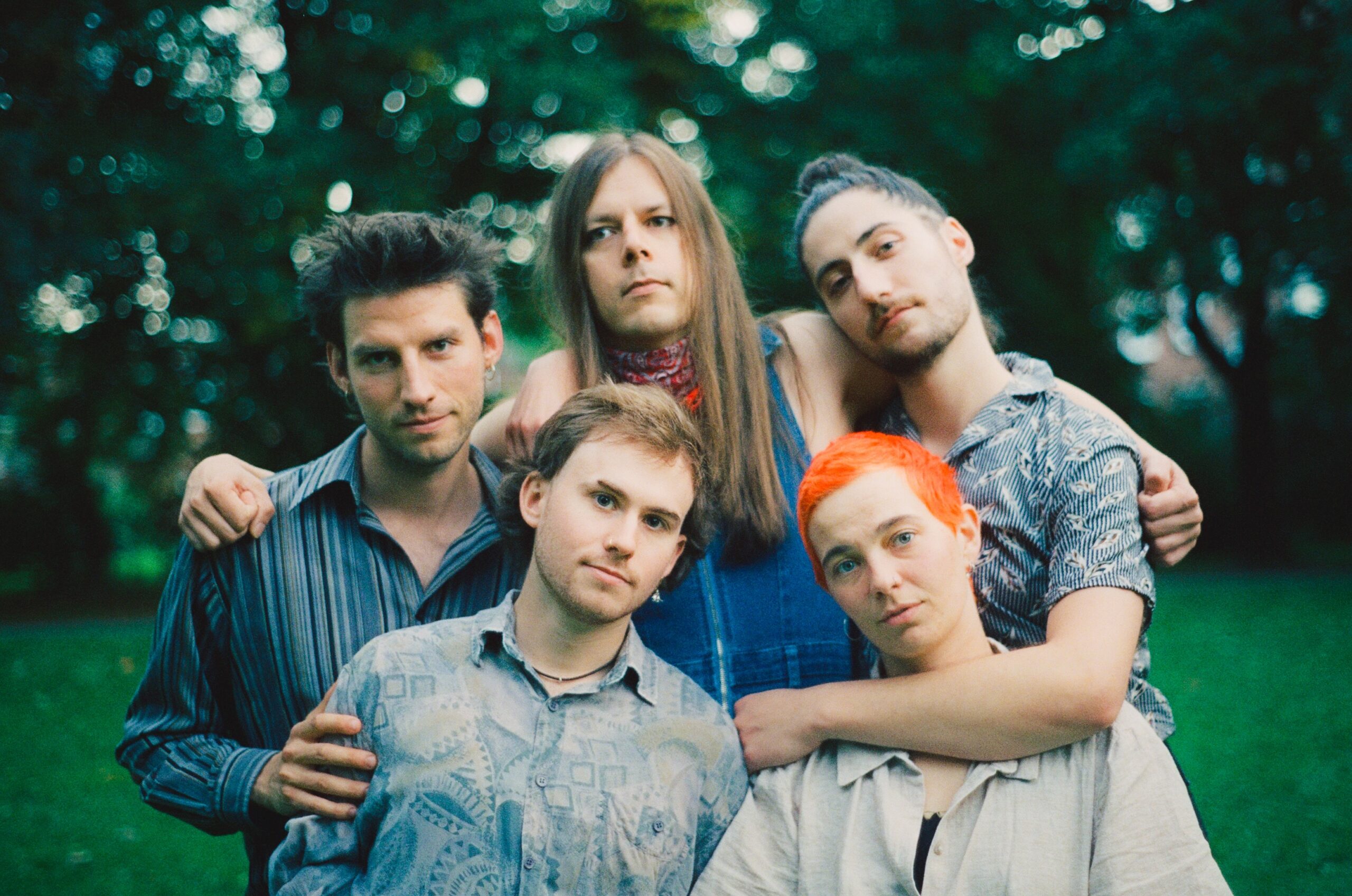 Fünf Personen draußen vor Bäumen, alle berühren sich und schauen in die Kamera