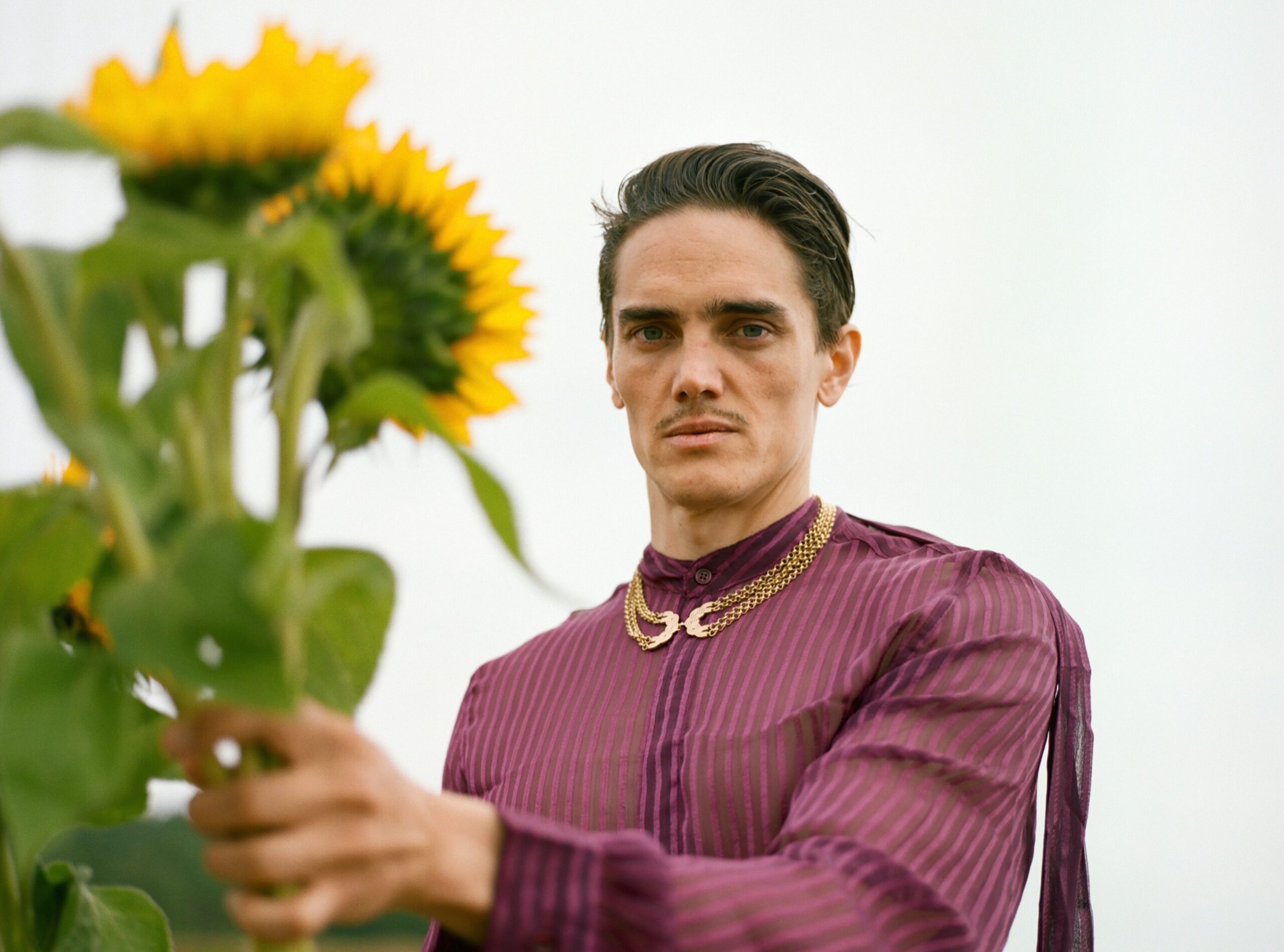 Ein Mann schaut in die Kamera, in einer Hand mehrere Sonnenblumen