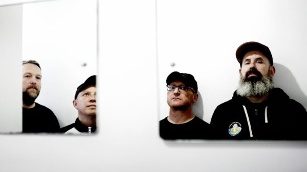 Vier Männer, man sieht sie nur über zwei Spiegel, die an einer weißen Wand hängen