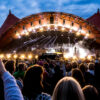 Besucher des „Roskilde“-Festivals feiern vor einer Bühne.
