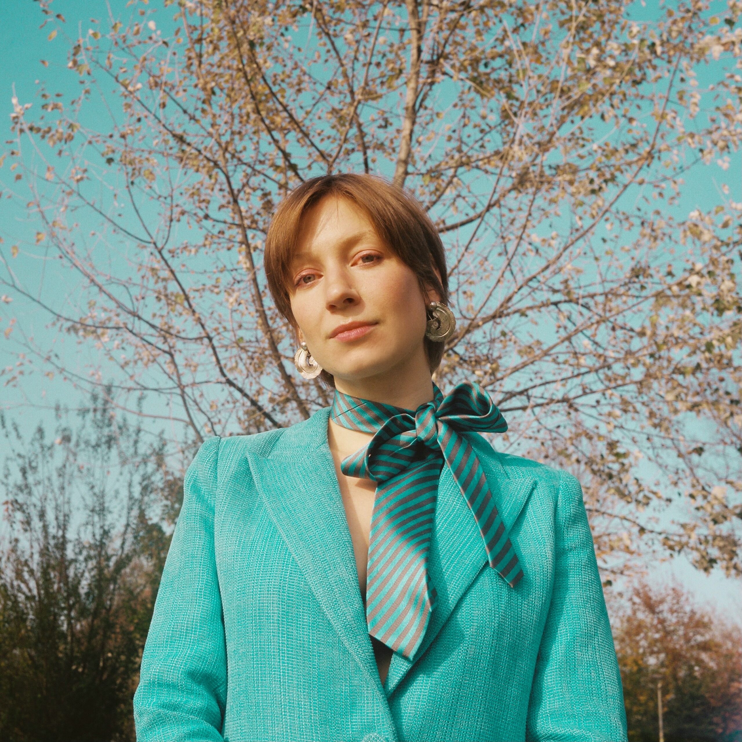 Eine Frau steht vor einem Baum und schaut in die Kamera