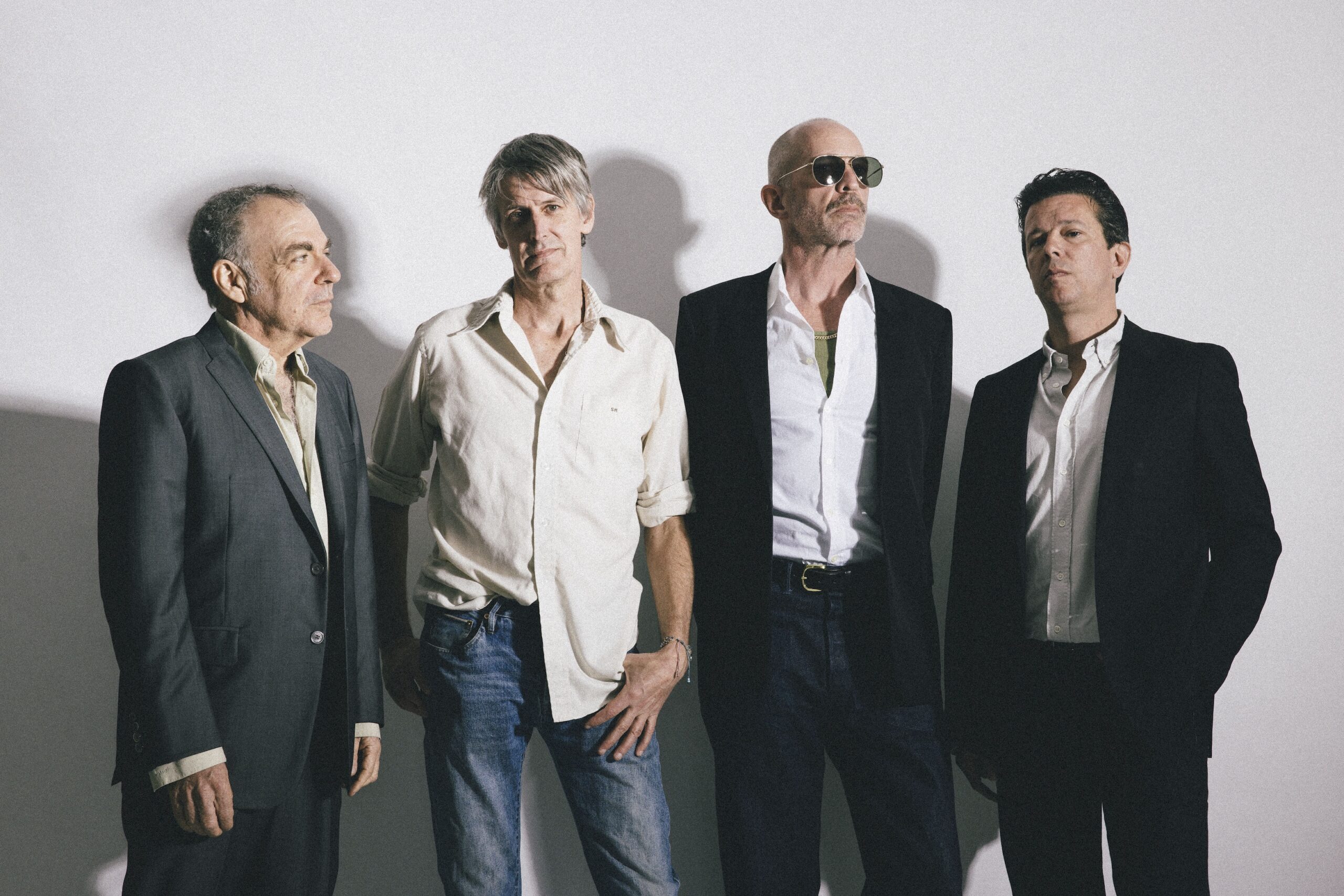 Vier Männer stehen vor einer weißen Wand, zwei schauen in die Kamera