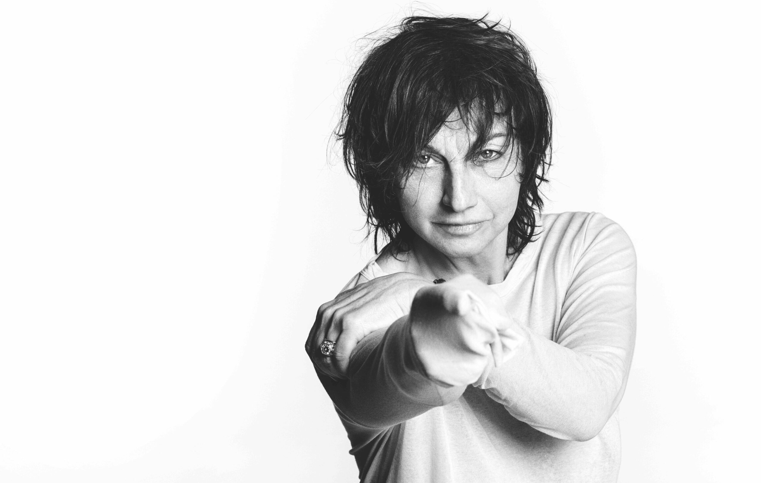 Schwarzweißfoto, sie lehnt sich ein bisschen nach vorne und zeigt mit dem Finger auf die Kamera