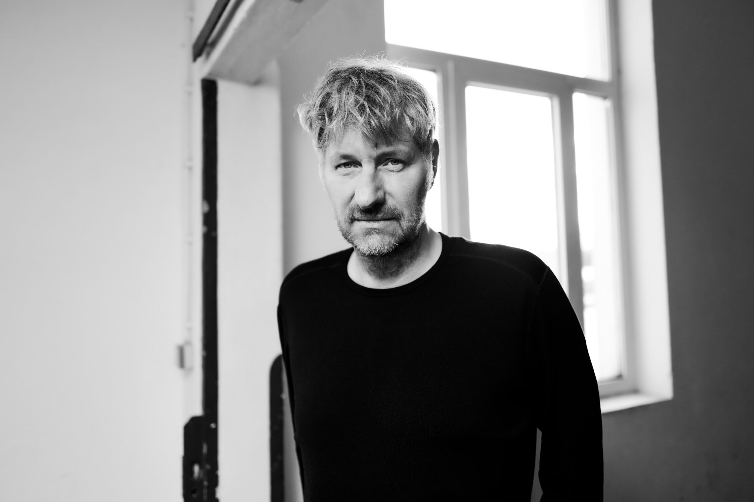 Schwarzweißfoto, er steht in einem leeren Raum und sieht in die Kamera