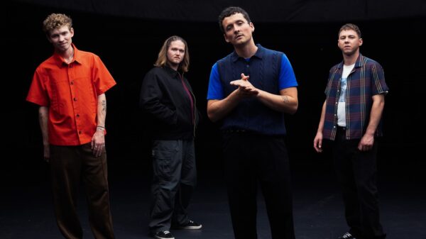 Vier Männer stehen vor einem schwarzen Hintergrund und schauen in die Kamera