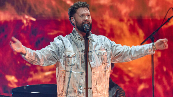 Er steht mit ausgebreiteten Armen am Mikrofon