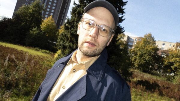 Er steht draußen, im Hintergrund Grün und Häuser