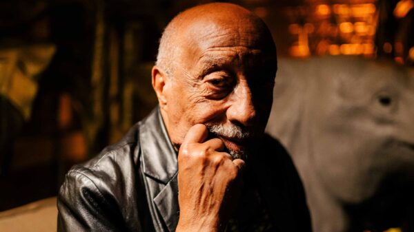 Er schaut in die Kamera, den Kopf auf eine Hand gestützt