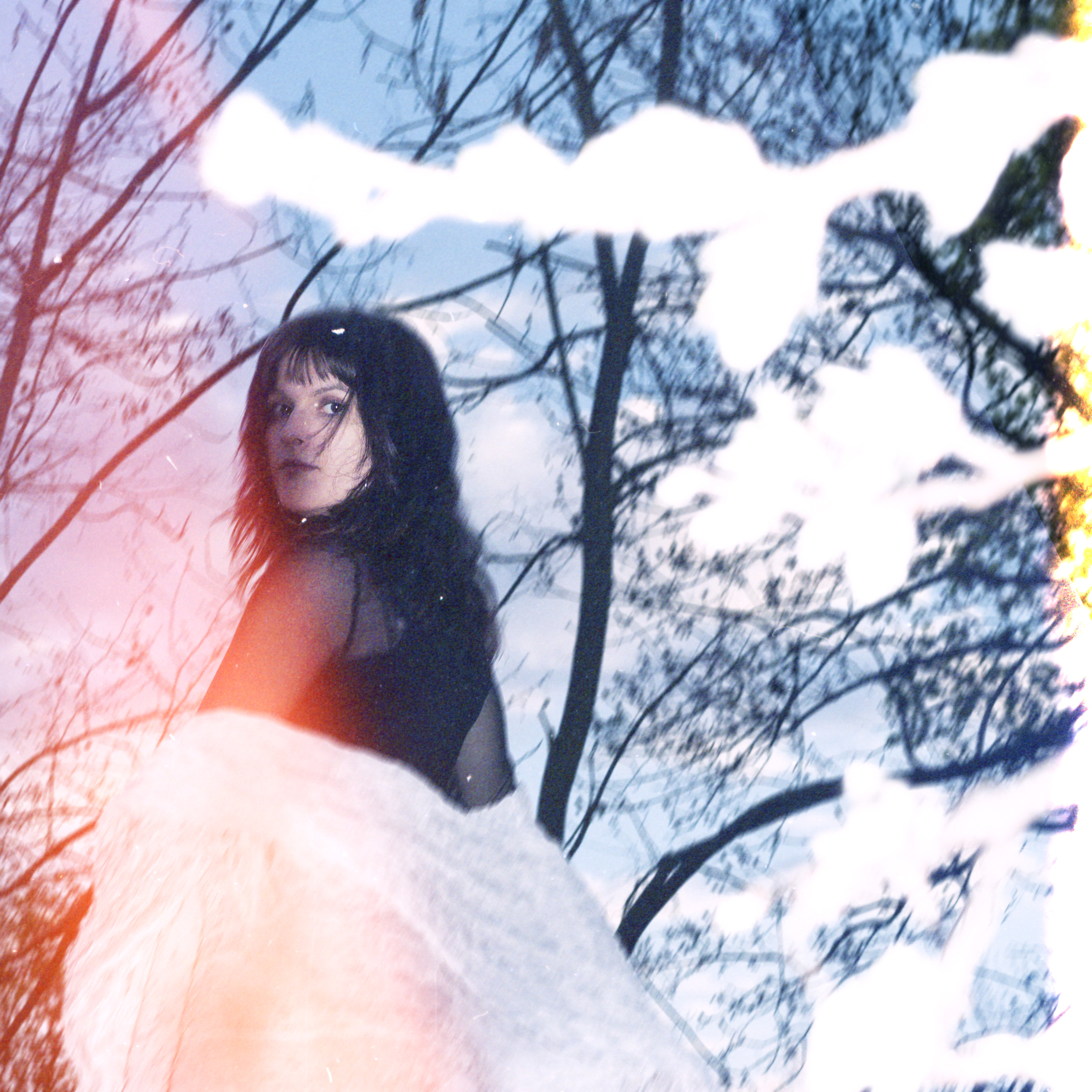 Draußen vor Bäumen ohne Blätter, sie schaut über ihre linke Schulter in die Kamera