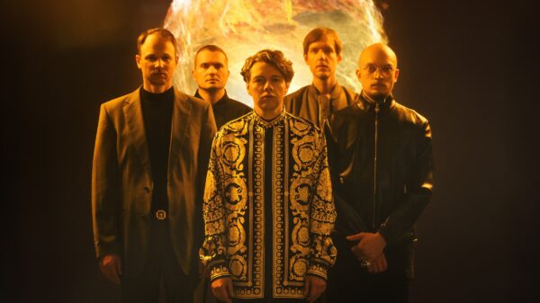 Fünf Männer stehen vor einer im Hintergrund angedeuteten Feuerkugel, vier tragen schwarze Kleidung, in der Mitte steht Christian Friedel in einem gemusterten Oberteil.