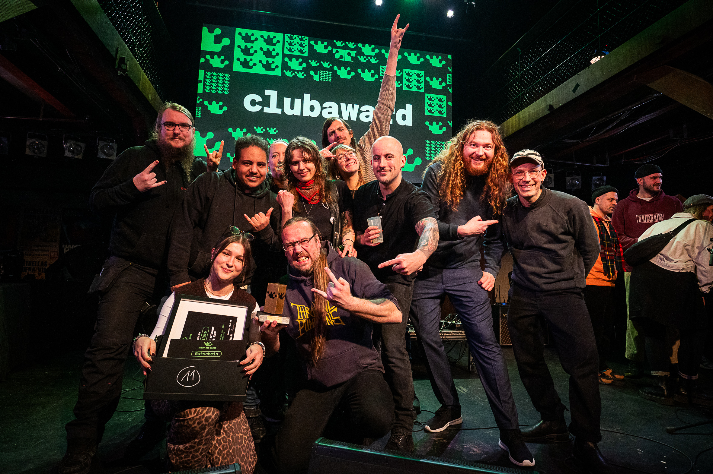 Viele lächelnde und lachende Menschen auf der Bühne, im Hintergrund steht auf einer Leinwand Clubaward