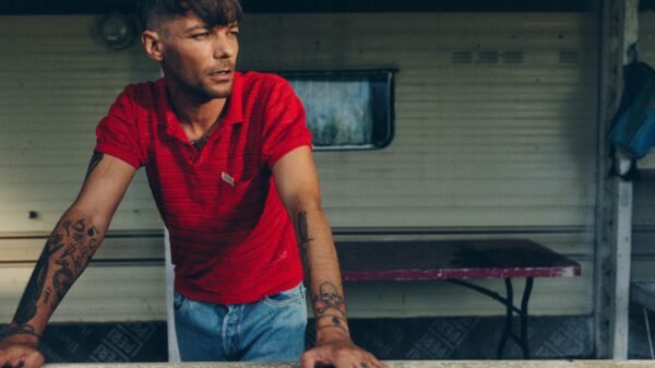 Er steht draußen, stützt sich vielleicht auf einen Tisch und schaut zur Seite