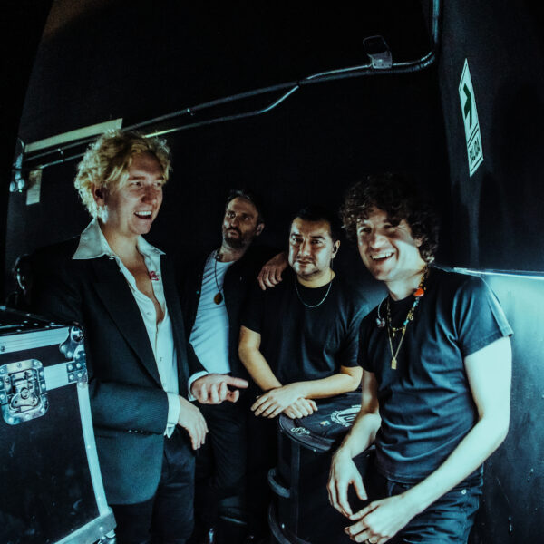 Dunkles Setting, vier Männer stehen nah beieinander, zwei von ihnen lachen, darunter auch Sänger Luke Pritchard, der rechts steht