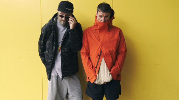 Die beiden Männer stehen vor einem gelben Hintergrund