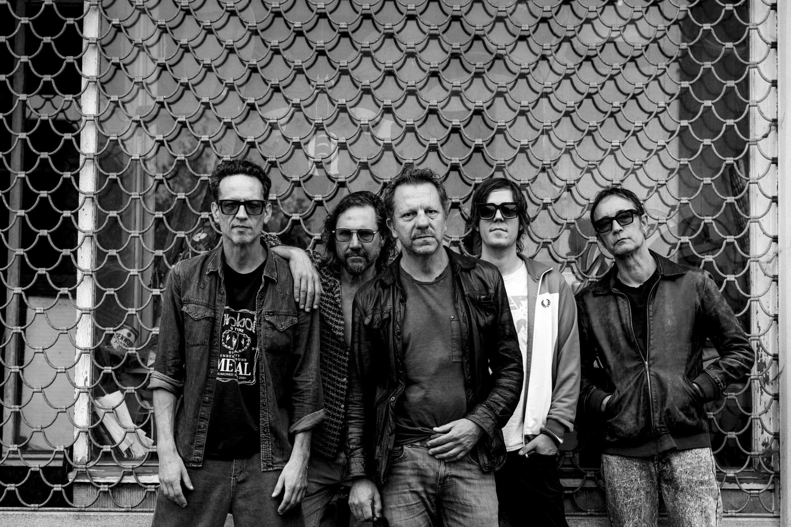 Fünf Männer stehen vor einem Schaufenster, vor dem ein Gitter runtergelassen ist. Bis auf Tom Barman tragen alle eine Sonnenbrille.