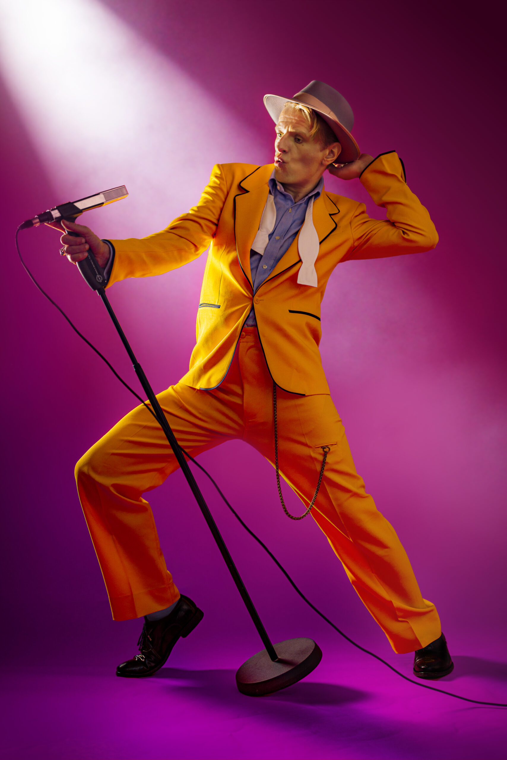Alexander Scheer steht in einem orangefarbenen Anzug an einem Mikrofon.