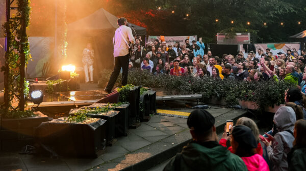 Band auf Open-Air-Bühne vor großem Publikum im Park bei Dämmerung.