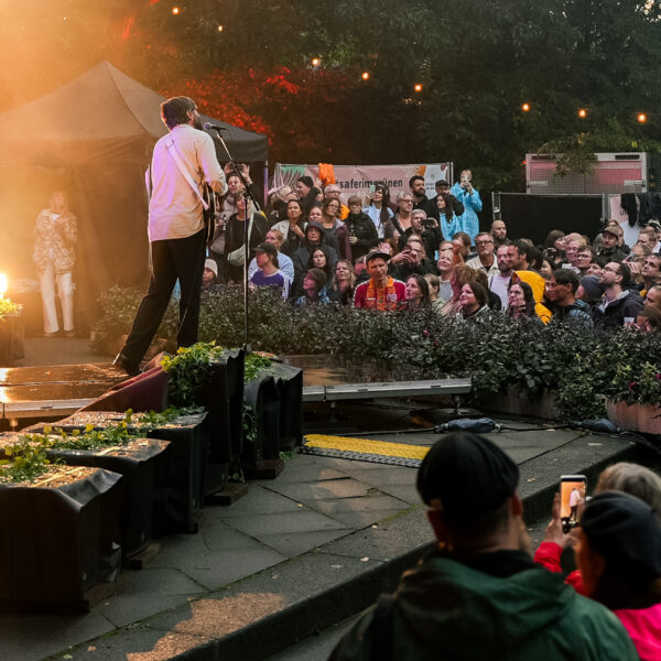 Band auf Open-Air-Bühne vor großem Publikum im Park bei Dämmerung.