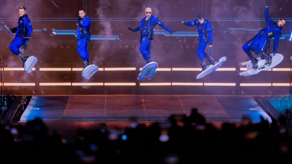 Die Backstreet Boys tanzen in blauen Outfits auf einer beleuchteten Bühne vor jubelndem Publikum.