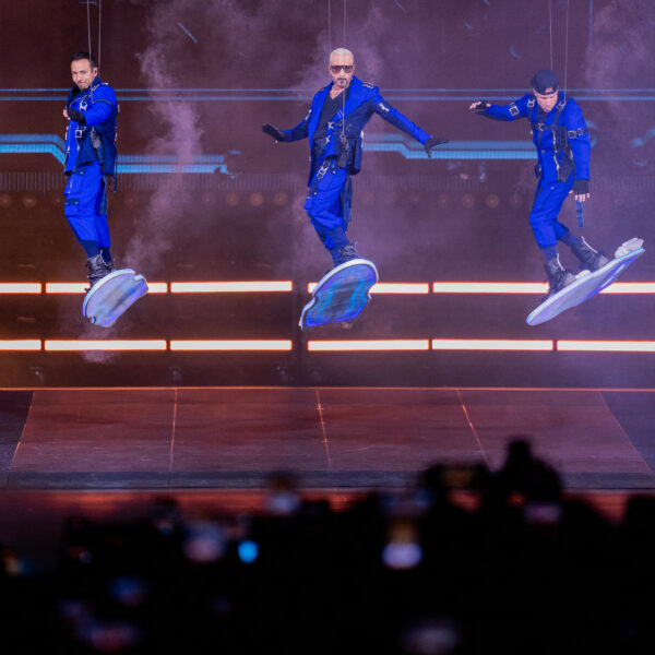 Die Backstreet Boys tanzen in blauen Outfits auf einer beleuchteten Bühne vor jubelndem Publikum.