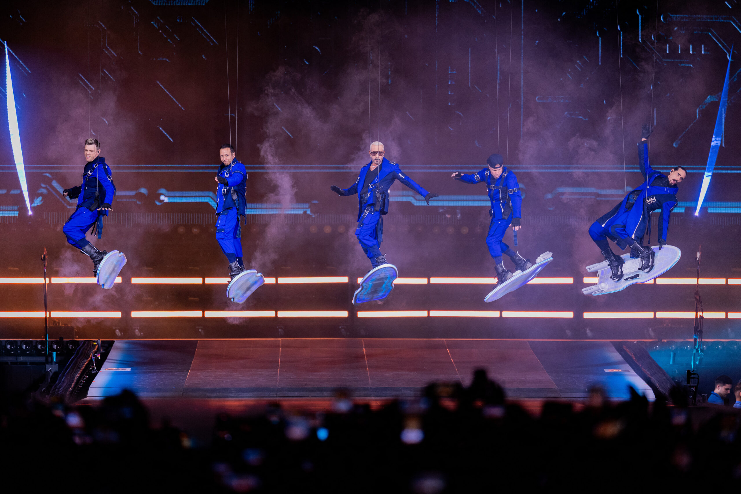Die Backstreet Boys tanzen in blauen Outfits auf einer beleuchteten Bühne vor jubelndem Publikum.