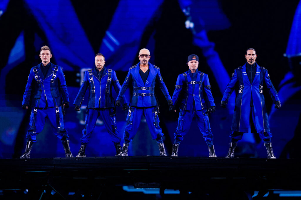 Die Backstreet Boys stehen in Formation in blauen Anzügen auf der Bühne.