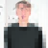 Frontalporträt eines Mannes mit schwarzem Oberteil vor hellem Hintergrund.